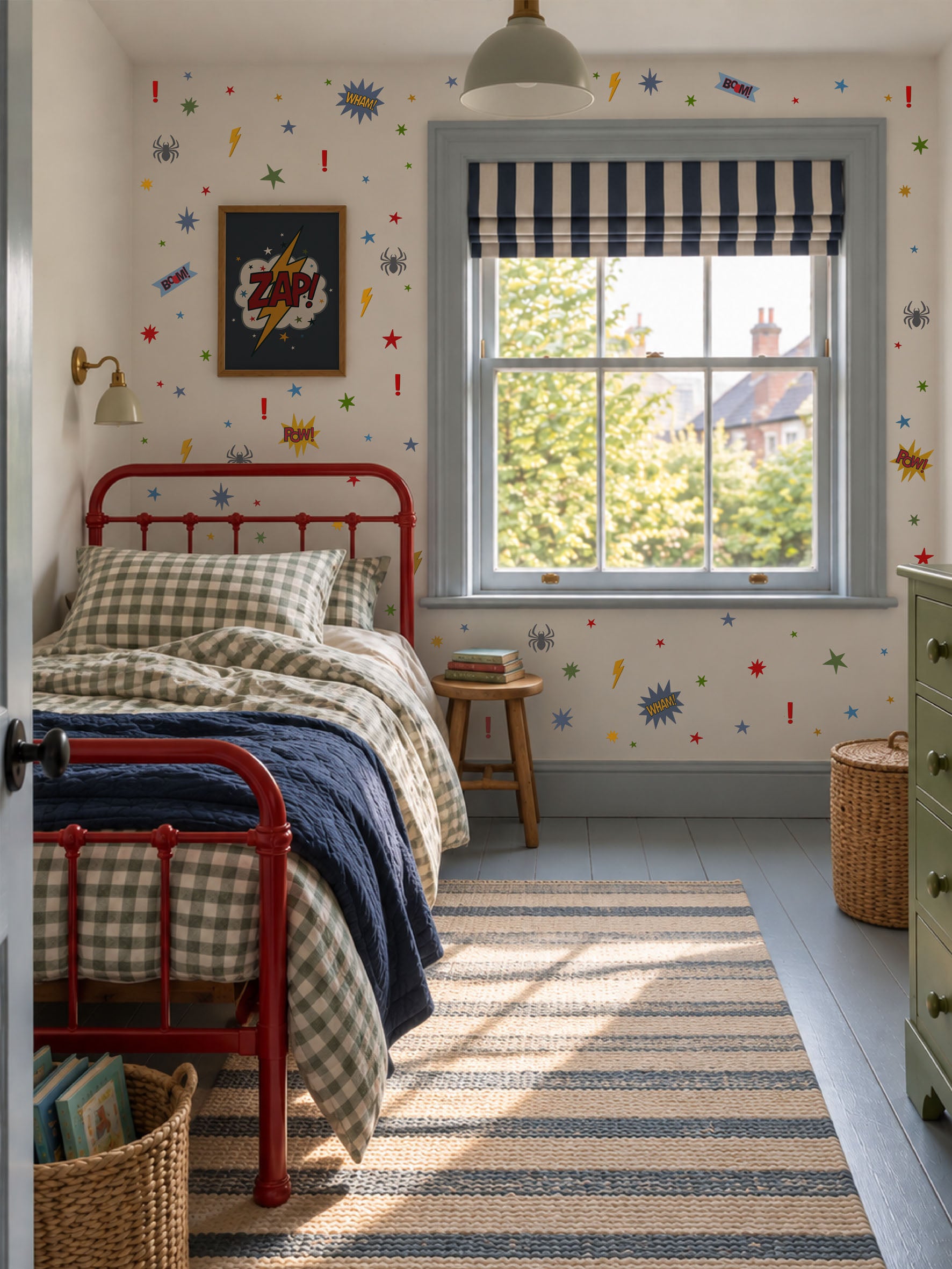 A styled children's bedroom featuring a red metal single bed with a gingham and navy blue bedding set, a striped navy and white roller blind, and colorful comic-book style starburst wallpaper decals on a white wall.