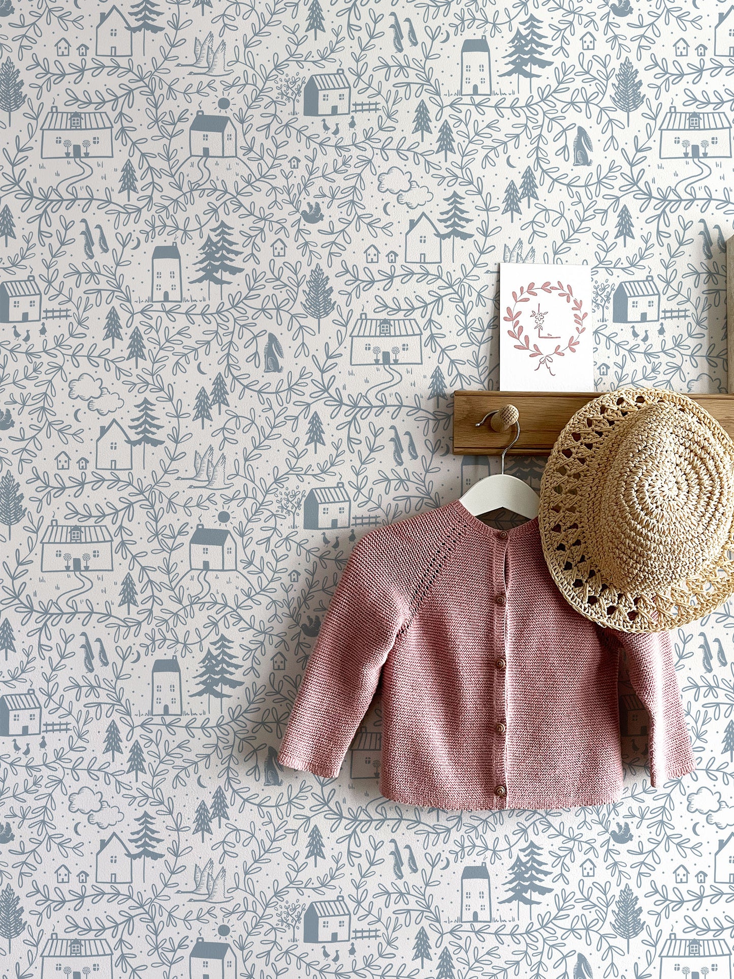 Cottages in the Woods blue dusk wallpaper with hooks, hanging pink baby cardigan and sun hat